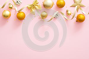 Bright glittering golden baubles, ribbon. stylish Christmas decorations top borer on pastel pink background. Christmas minimal