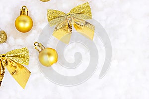 Bright golden and yellow Christmas decorations ribbons, baubles, ornament flat lay on white artificial snow background with copy