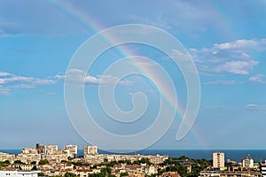 Bright gorgeous rainbow in a blue sky over seashore city and sea. Multicolored rainbow against a clear blue sky on a sunny day.