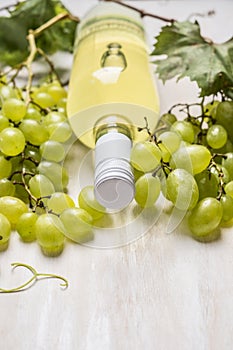 Bright grapes with bottle of white wine and vine leaves on a white wooden background, close up