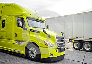 Bright green big rig semi truck with grille guard standing on truck stop beside with another trucks with semi trailers