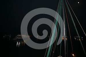 Bright green boat rigging  against the black of night sky with tourst boats lights reflecting of water in background