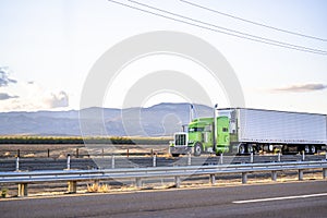 Bright green classic big rig semi truck tractor transporting cargo in refrigerator semi trailer driving on the flat road in