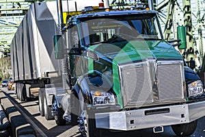 Bright green day cab big rig semi truck transporting cargo in tented dry van semi trailer driving on the truss bridge at sunny day