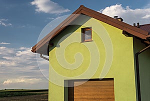 A bright green facade of the house with a visible roof soffit, window and garage door. In the background a nice blue sky with clou