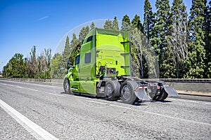 Bright green powerful big rig semi truck tractor without the semi trailer running on the wide highway road to warehouse for pick