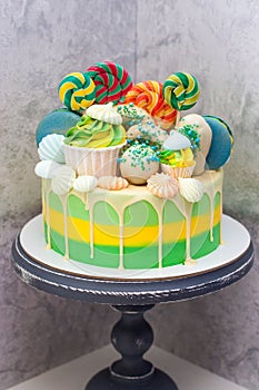 Bright green and yellow cake with lollipops, macaroons, meringues and melted chocolate