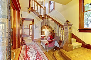 Bright hallway with colourful rug, nice red sofa, wooden staircase and beige carpet covered steps