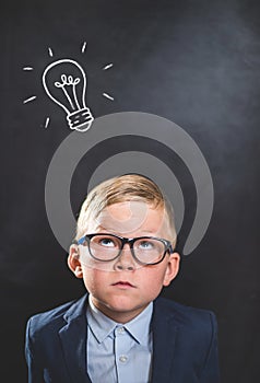 Bright idea. Nerd little kid boy with illustrated bulb above his head against blackboard. Back to school