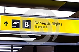 Bright illuminated yellow and black airport signs with arrows and plane icons and the title in Chinese: Domestic flights.