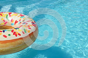 Bright inflatable doughnut ring floating in swimming pool on sunny day