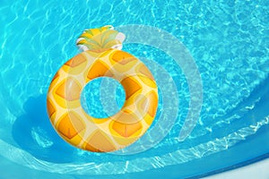 Bright inflatable pineapple ring floating in swimming pool on sunny day, above view