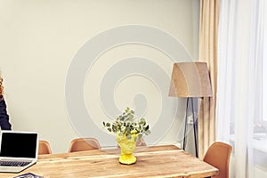 The bright interior of the office space with dried flowers and a laptop. A black laptop screen on a wooden office table