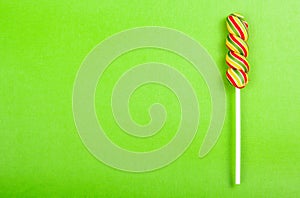 Bright juicy colored lollipop on a green paper background. Lollipop in the form of a color spiral. Fruit candy.