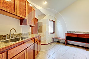 Bright kitchen room interior with brown storage cabinets, granite counter top and tile floor.