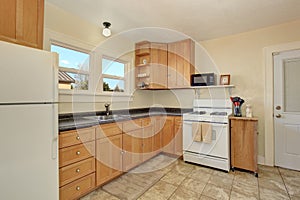 Bright kitchen room interior with honey color cabinets and tile floor.