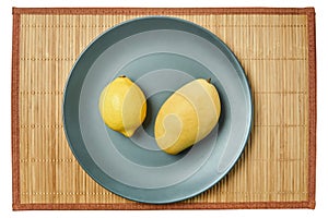 Bright lemon and yellow mango on a gray plate on a cane tablecloth