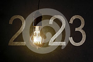 Bright light bulb with number 2023 on concrete wall