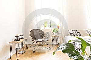 Bright light shining through a window into a modern bedroom interior with a rattan and metal chair, bedside stand with candles