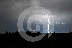 A bright lightning bolt with many side branches strikes down to earth.