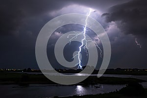 Bright lightning bolt with many side branches strikes down to earth in a river landscape