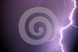 Bright lightning discharges in the stormy sky under dark violet rain clouds photo