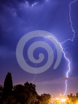 Bright lightning sparkles with a beautiful pattern in the evening sky over the city and trees