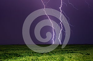 Bright lightnings in dark stormy sky above green field, climate change or weather forecast concept image