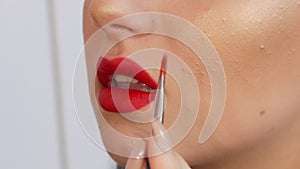 Bright lip makeup, big beautiful lips are painted with red lipstick with a special brush in a beauty salon. Professional