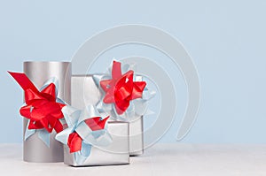 Bright metallic paper gift boxes with red and blue satin ribbons and bows on soft light white wood board.