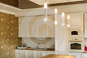 Bright modern cylinder illuminators hanging from the ceiling. Kitchen room on the background photo