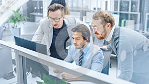 In Bright Modern Office: Young Businessman Sitting and Working at His Desktop Computer with Projec