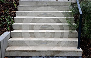 Bright monolithic concrete park staircase with stair lighting with metal railing black interlocking paving, bushes slope