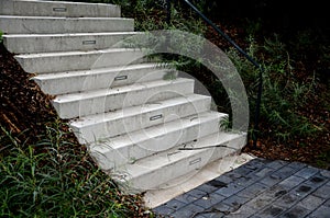 Bright monolithic concrete park staircase with stair lighting with metal railing black interlocking paving, bushes slope