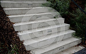 Bright monolithic concrete park staircase with stair lighting with metal railing black interlocking paving, bushes slope