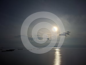 Bright moonlight and sparkling starlight in the sky above a beach of calm waters with several ships