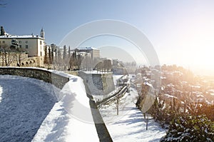 Bright morning sunshine bursting over a snow-covered  Italian landscape, with a road, wall, trees and buildings, in the old city o