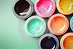 Bright, mother-of-pearl, multicolored open cans of paint on a bright green background. View from above. The concept of creativity