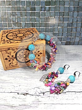 Bright multi-colored bracelet and earrings made of turquoise and mother of pearl with a wooden box on a bright table.