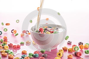 Bright multicolored breakfast cereal in bowl with pouring milk