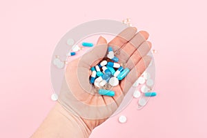 Bright multicolored pills in women hand on pink background. Female hands holding various colorful pills, capsules, tablets. Flat