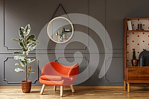 Bright orange armchair, a retro wooden cabinet and a mirror on a