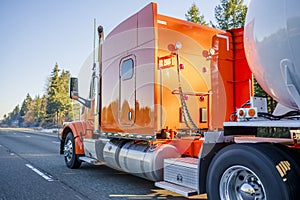 Bright orange big rig semi truck transporting tank semi trailer for transportation of liquid and liquefied chemical cargo running