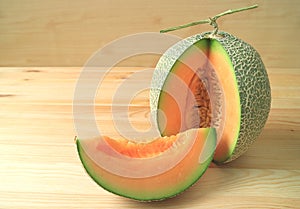 Bright orange color juicy ripe cantaloupe melon sliced from whole fruit isolated on wooden table