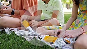 Bright orange corn cobs in foil at a picnic in the park in the hands of vacationing children.