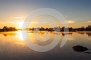 Bright orange dawn warm rays dispel mist over a calm river, illuminating the light in the area. photo