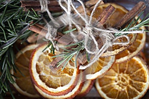 Bright orange dried round orange slices on a wooden board with cinnamon sticks, fir branches, ingredients for cooking or Christmas
