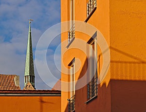 Bright orange facade of modern residential building lit by the evening sun with church spire in the background