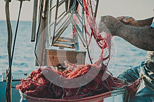 Bright orange fishing net with floats. Fisher boat in a sea. Hands of an old fisherman