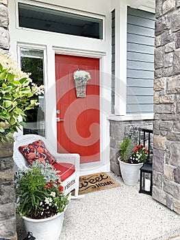 Bright orange front door and porch with a wicker chair. Colorful entrance